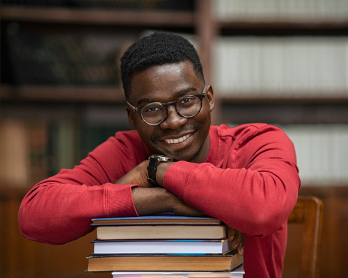 African American male student smiling and leaning on a stack of books 